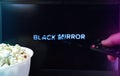 Person watching Black Mirror series with popcorn and a remote control. Stock editorial photo.