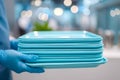 Person wearing blue gloves holding a stack of clean light blue rectangular plates in a brightly lit modern kitchen environment Royalty Free Stock Photo