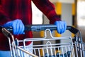 Person wearing blue protective surgical latex rubber gloves pushing shopping cart trolley