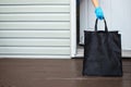 A person wearing gloves, picking up a groceries bag from a home entrance