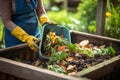 Person wearing gloves throwing food and yard scraps into a residential compost bin. Decomposing organic matter rich in nutrients