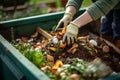 Person wearing gloves throwing food and yard scraps into a residential compost bin. Decomposing organic matter rich in nutrients