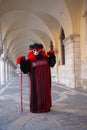 Person wearing a Venetian mask and a black and red costume under arches of Doges Palace at the Venice Carnival in Venice Italy Royalty Free Stock Photo