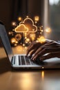 A person is working on a laptop displaying a cloud icon, with a potted plant sitting on the table next to it, creating a Royalty Free Stock Photo