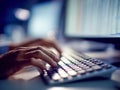Person working late on a computer keyboard in a dimly lit office environment with multiple screens displaying data and information Royalty Free Stock Photo