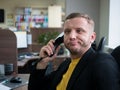 Person is working too hard, his face displays sign of exhaustion. Midlife man sitting in the office and talking on the phone