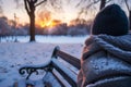 person wrapped in woolen scarf watching sunset from snowcovered park bench