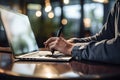 a person writing on a notebook and sitting near a laptop