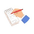 A person is writing on a notepad with a red pen