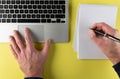 Person writing on notepad while working on laptop computer Royalty Free Stock Photo