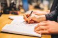 Person writing notes in a notebook with a pen at a wooden desk in a focused setting Royalty Free Stock Photo