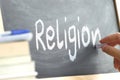 A person writing the word Religion on a blackboard.