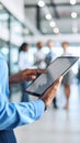 Person's hands using a tablet computer in a modern office setting with colleagues blurred in the background. Royalty Free Stock Photo