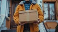 Person in a yellow coat delivering a taped cardboard box at a doorstep.