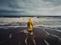 A person in a yellow raincoat standing on a beach. AI generative image.