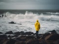 A person in a yellow raincoat standing on rocks near the ocean. AI generative image.