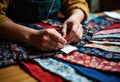 Person sewing colorful patterned fabric with a needle and thread on a wooden Royalty Free Stock Photo