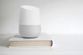 Personal assistant loudspeaker on a white wooden shelf of a smart home living room. Next, a book. Empty copy space Royalty Free Stock Photo