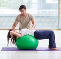 Personal coach helping woman in gym with stability ball