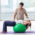 Personal coach helping woman in gym with stability ball