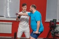 Personal fitness trainer shows to a fat man how to perform an exercise with dumbbells in a gym. Overweight