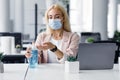 Personal hygiene in modern office after lockdown. Attractive woman in protective mask and smart watch disinfect hands