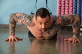 Personal trainer with tattoos performs exercises with his arms in the gym.