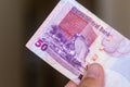 Persons hand giving the Currency of the Qatar - One fifty rial or riyal note spread out on a brown background. Money exchange