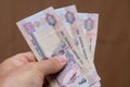 Persons hand giving the Currency of the United Arab Emirates UAE - Five hundred Dirham notes spread out on a brown background.