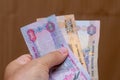 Persons hand giving the Currency of the United Arab Emirates UAE - Multiple hundred Dirham notes spread out on a brown Royalty Free Stock Photo