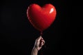 A persons hand holding a bright red heart-shaped balloon against a clear blue sky, A heart balloon held in a clenched fist, Royalty Free Stock Photo