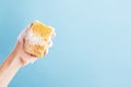 Persons hand holding yellow sponge for dish wash. Washcloth covered in soap. Domestic chores and supplies concept. Sensitive