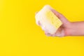 Persons hand holding yellow sponge for dish wash. Washcloth covered in soap. Domestic chores and supplies concept. Sensitive