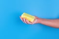 Persons hand holding yellow sponge for dish wash. Washcloth covered in soap. Domestic chores and supplies concept. Sensitive