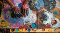 A persons hands covered in paint using a variety of brushes and tools to make different patterns on a large canvas. The Royalty Free Stock Photo