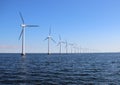 Perspective line of ocean wind mills with dark water and sky