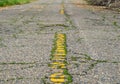Old road with yellow lines and lots of cracks with grass growing