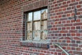 Perspective shot of an old industrial window with broken glas, behind it is covered with a wood board, old red brick wall with