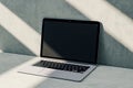 Perspective view on blank dark modern laptop monitor with place for logo brand or web design on sunlit concrete wall background Royalty Free Stock Photo