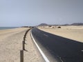 Perspective view of curved asphalt road between sand dunes, volcanic and desert landscape and calm ocean. Lonely road in Idyllic Royalty Free Stock Photo