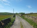 Perspective view of a a long narrow country road surrounded by stone walls and flowers in west yorkshire countryside surrounded Royalty Free Stock Photo