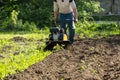 Perspective view of man plowing garden soil by motor cultivator