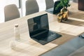 Perspective view on modern laptop on wooden table with glass of water and golden vases in sunlit office. 3D rendering