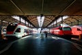 Perspective view of a platform in Lucerne Central Railway Station with sunlight cast on trains parking by the platform & passenger