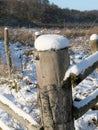 Perspective view of round wooden posts of a wooden fence covered with snow hoods Royalty Free Stock Photo