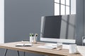 Perspective view on stylish work place with wooden table, modern computer monitor, white coffee mug and notebook on grey wall Royalty Free Stock Photo
