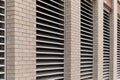 Perspective view of wall of an urban commercial building with numerous inset HVAC air exhaust vents, light colored brick