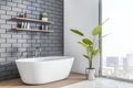 Perspective view on white bath in stylish sunlit bathroom with white bath on grey brick wall background, wooden and concrete floor Royalty Free Stock Photo