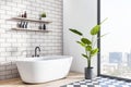 Perspective view on white bath in stylish sunlit bathroom with white bath on light brick wall background, wooden and mosaic floor Royalty Free Stock Photo