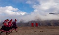 Three indigenous women walk in front of cloud covered mountain range wearing traditional